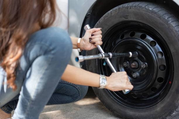Woman using a tyre spanner to change a car tyre safely in Johannesburg